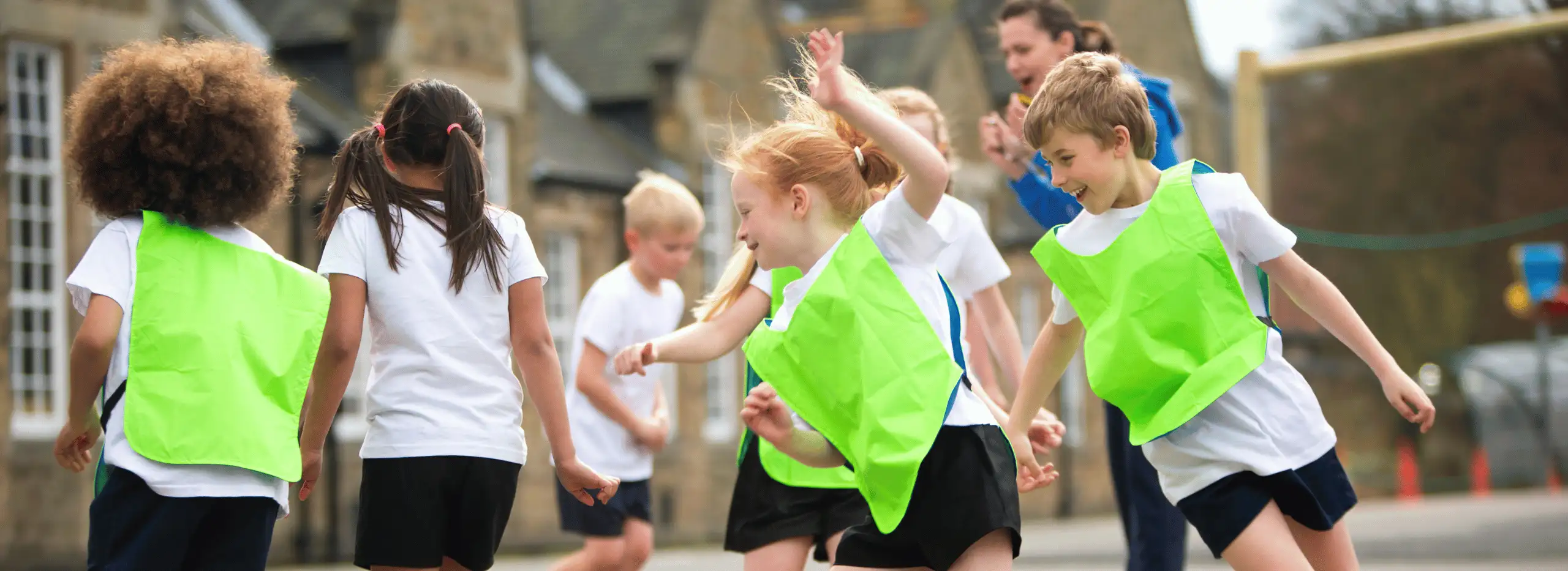 Level-3-Teaching-Assistant-Apprenticeship-PE-Health-Wellbeing-Focus A group of children doing PE in the playground with a young apprentice
